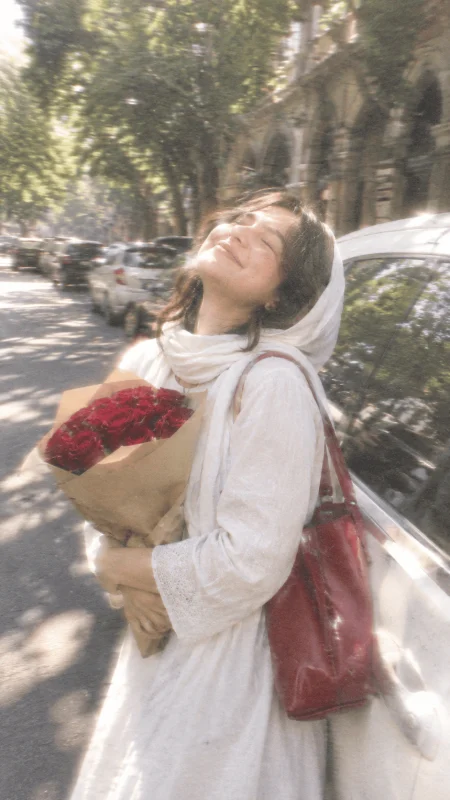 Dreamy girl holding red roses beside a vintage car on a sunny street