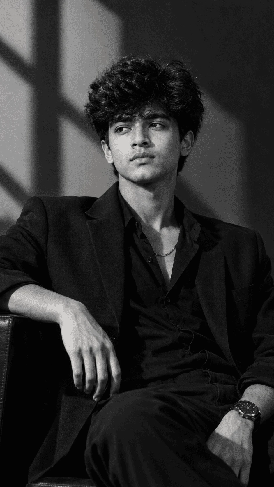 Black and white luxury fashion portrait of a young man sitting in a chair